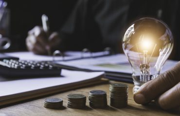 Hand of male holding a light bulb with stack of coins for accoun